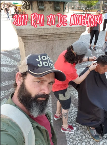 O pai do Felipe em primeiro plano na Rua XV de Novembro, em 2017, com um corte de cabelo acontecendo ao fundo